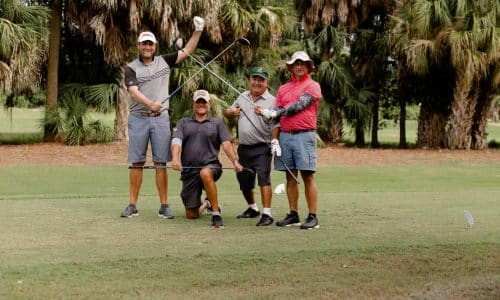 4 men posing on a golf course with their clubs