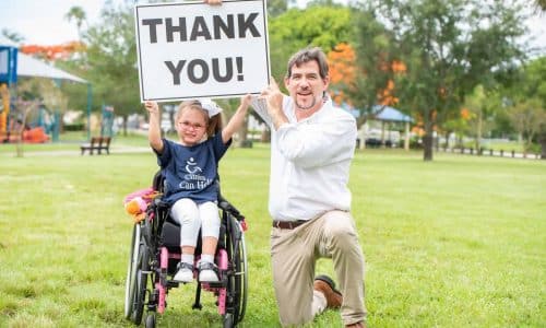 young child in wheelchair and adult male holding a sign together that says Thank You!